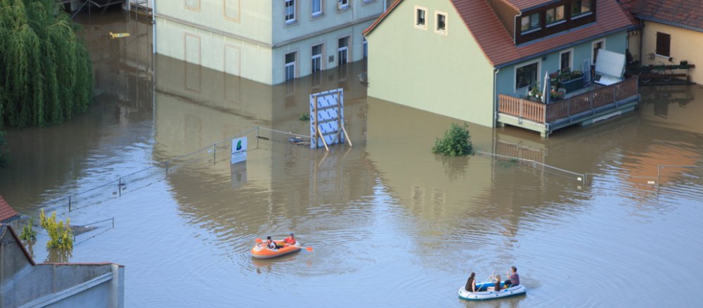 Menschen rudern in Schlauchbooten über das Wasser. Blick von Oben auf die Überschwemmung.