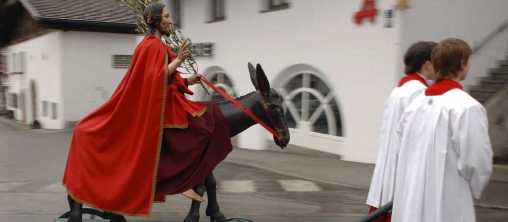 Zwei Ministranten ziehen am Palmsonntag einen hölzernen Esel mit Christusfigur.