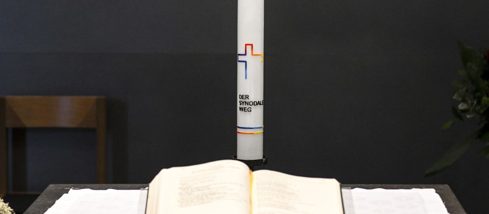 Kerze mit Logo und Aufschrift "Der Synodale Weg" hinter einem Messbuch.