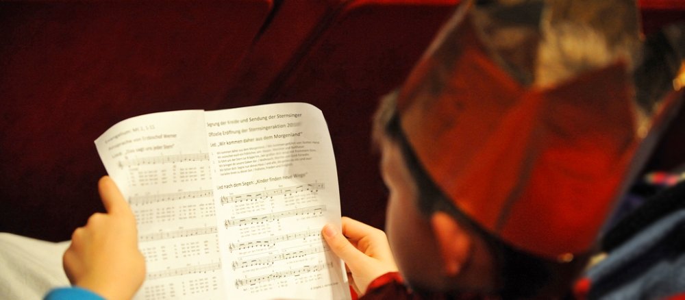 Sternsinger sitzt in einer Kinositzreihe und liest in einem Liedblatt.
