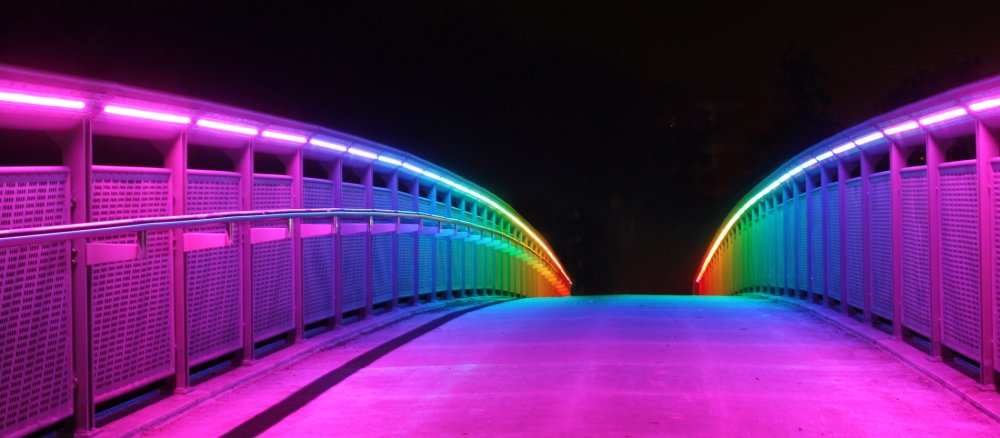 Eine Brücke, die nachts in Regenbogenfarben beleuchtet ist.