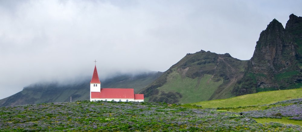 Die Dorfkirche des Ortes Vik i Myrdal im süden Islands vor nebelverhangenen Bergen.