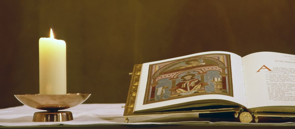 Reich bebilderte Bibel auf dem Altar. Daneben brennt eine Kerze.