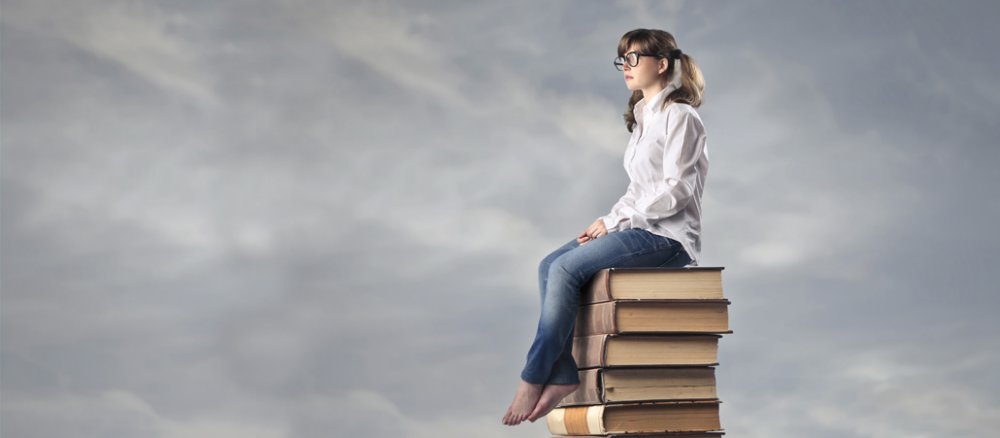 Ein Mädchen sitzt auf einem Bücherstapel.