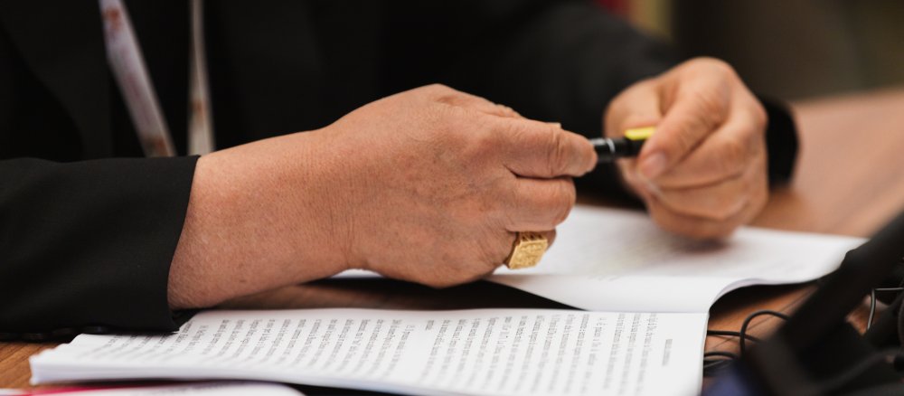 Ein Bischof schließt einen Stift, unter seinen Händen liegt das Abschlussdokument der Weltsynode