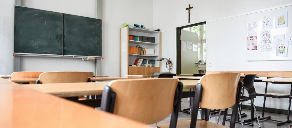 Tische und Stühle stehen in einem Klassenraum im Aloisiuskolleg in Bonn am 8. Juli 2019. Über der Tür hängt ein Kruzifix.