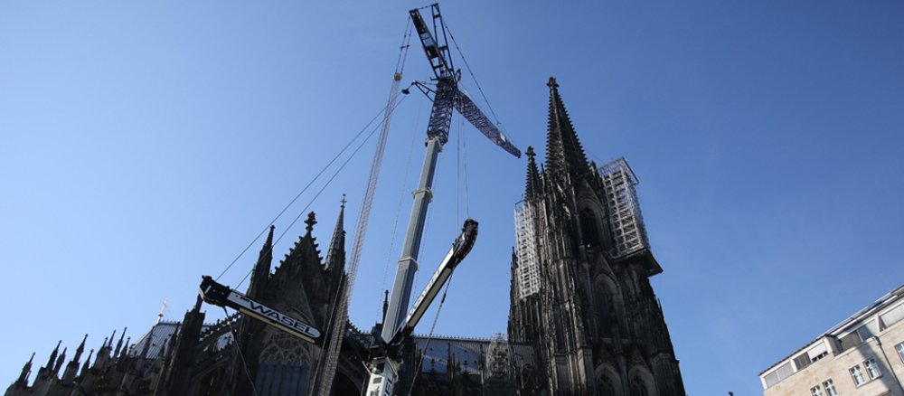 Ein Kran steht am 22.07.2013 in Köln (Nordrhein-Westfalen) vor dem Dom und hängt von dort aus eine Baugerüst ab.