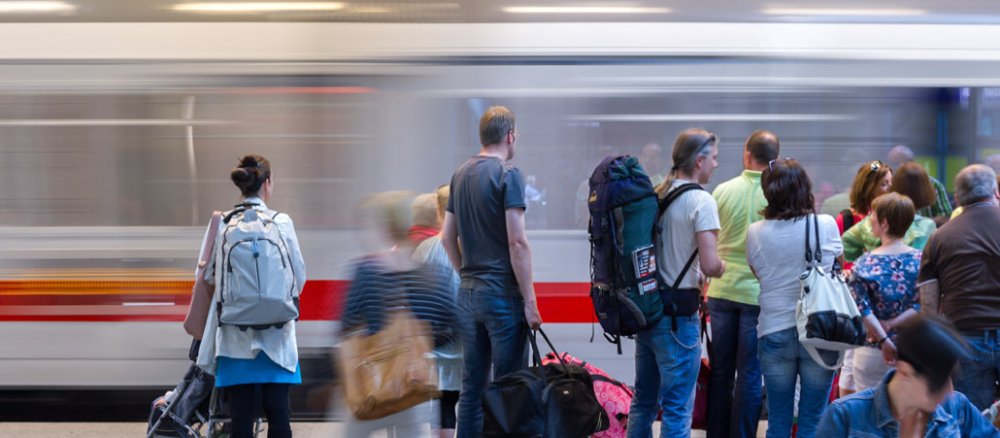 Reisende warten an einem Bahnsteig.