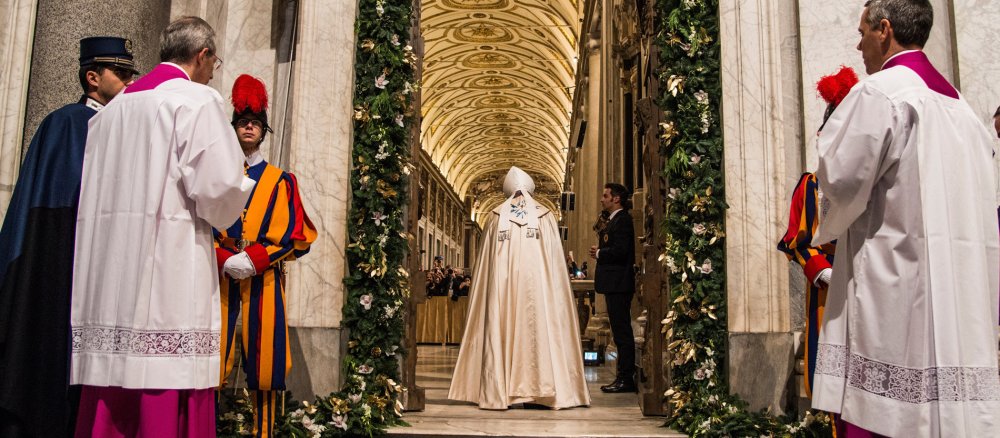 Papst Franziskus schreitet durch eine festlich geschmückte Tür.