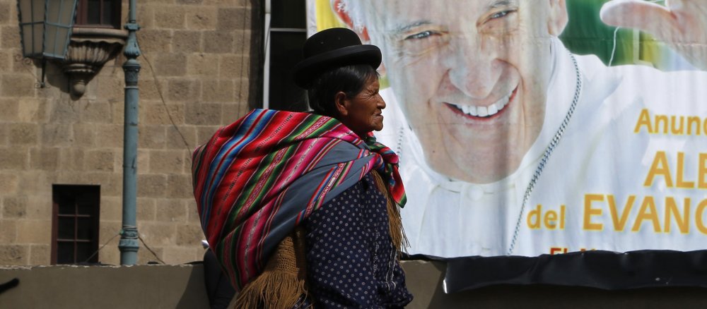 Eine bolivianische Frau läuft in der Stadt La Paz an einem Plakat vorbei, das den Besuch von Franziskus ankündigt.