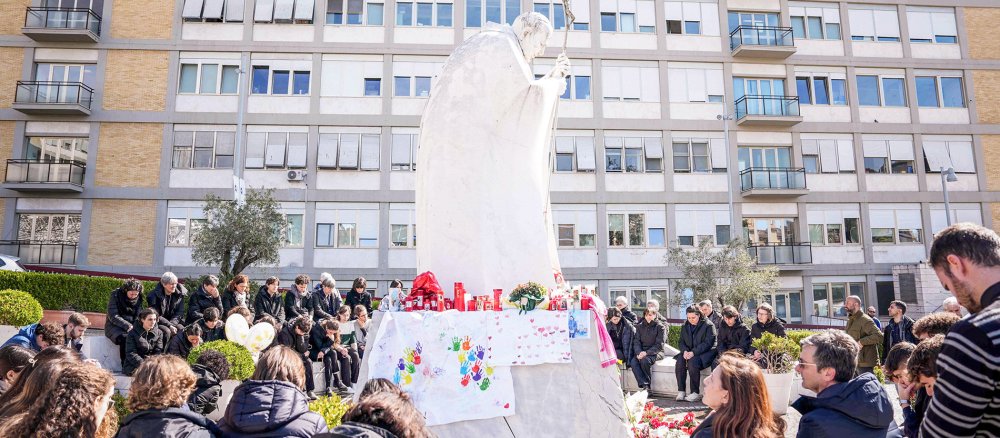 Menschen stehen und sitzen vor dem Gemelli-Krankenhaus in Rom.