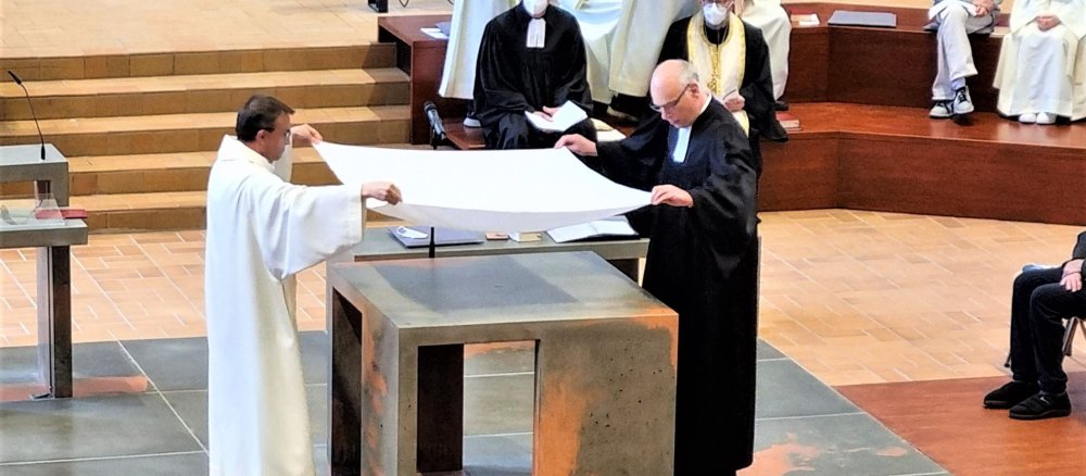 Ein katholischer und ein evangelischer Pfarrer breiten gemeinsam ein Altartuch aus