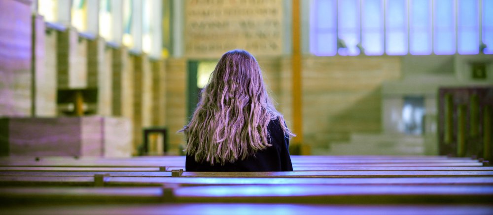 Eine junge Frau sitzt in einer Kirchenbank.