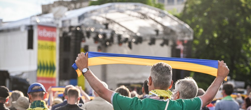 Ein Teilnehmer des Katholikentags steht in der Menge vor der Bühne und hält einen gelb-blauen Schal