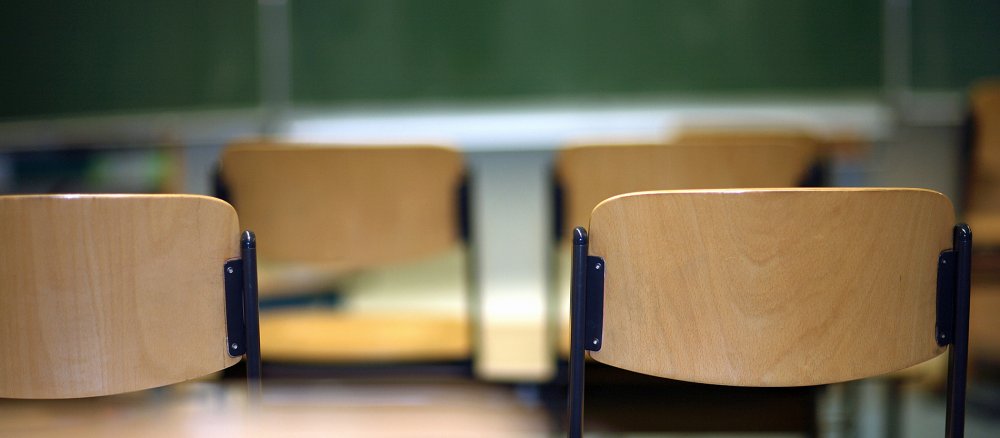 Leere hochgestellte Stühle in einem Klassenraum deuten auf das Ende des Unterrichts.
