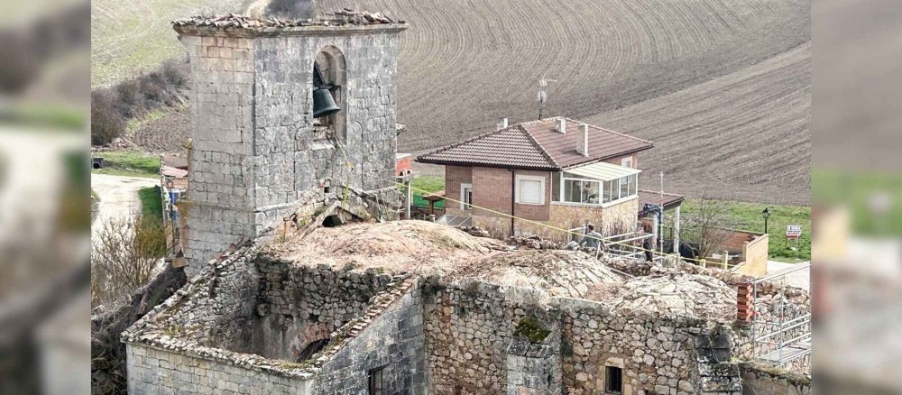 Der steinernen Kirchenruine fehlt das Dach. Im Turm hängt noch eine Glocke.