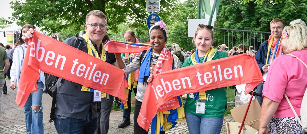 Teilnehmer halten rote Schals mit der Aufschrift: "Leben teilen" in die Höhe