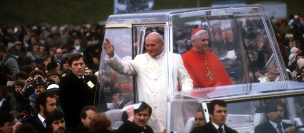 Papst Johannes Paul II. begrüßt die Menschen aus einem weißen Papamobil