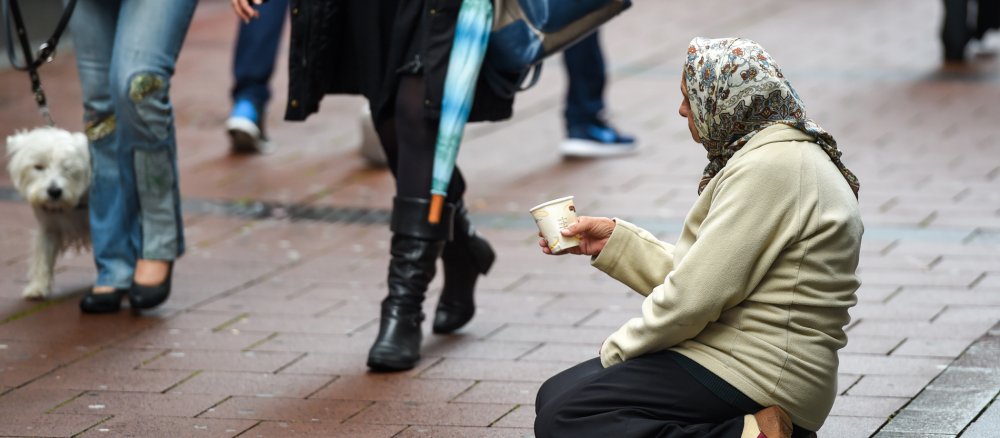 Eine Bettlerin sitzt auf dem Pflaster in der Fußgängerzone in Bonn. Passanten gehen an der Frau vorbei.
