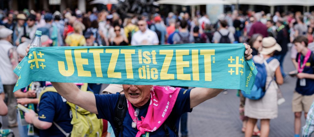 Eine Frau hält den Schal mit dem Kirchentagsmotto "Jetzt ist die Zeit" hoch