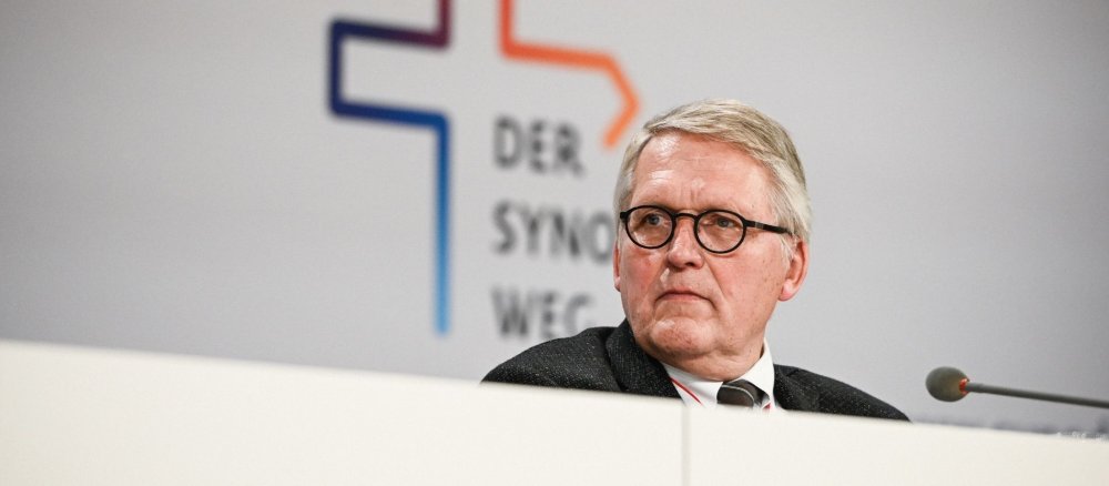 Thomas Sternberg sitzt vor einem Mikrofon, im Hintergrund das Logo des Synodalen Wegs.