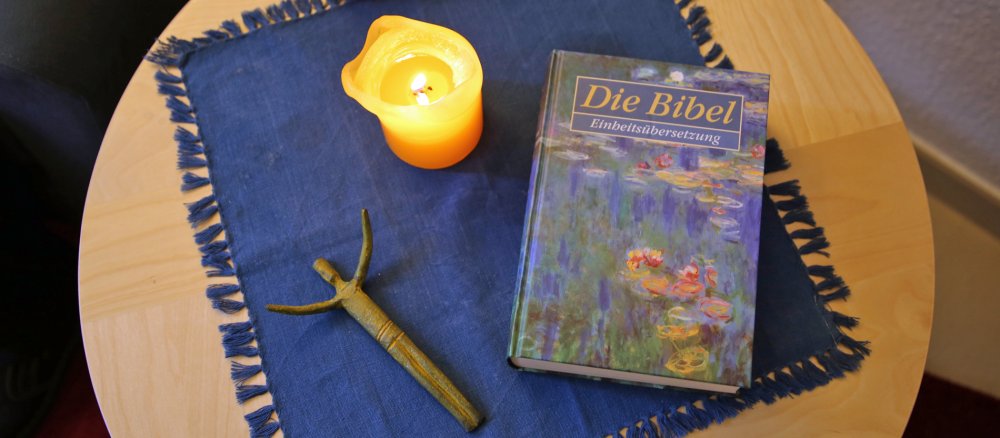 Eine Bibel, eine Kerze und ein Kreuz liegen auf dem Tisch.