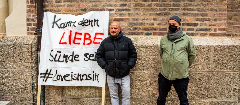 Kirchenpfleger Stephan Alof und Pfarrer Rainer Maria Schießler neben einem Plakat