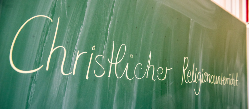 Der Schriftzug "Christlicher Religionsunterricht" steht am 1. Juli 2026 in einem Klassenraum in Hildesheim an einer Tafel.