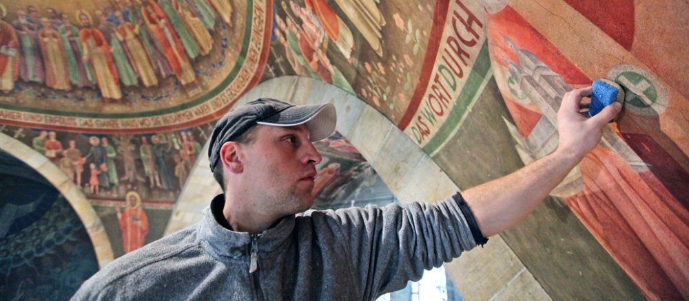 Ein Handwerker schruppt mit einem Spezialschwamm über ein Wandgemälde.