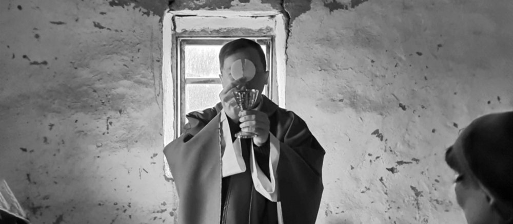 Ein Priester steht mit der erhobenen Hostie vor dem Gesicht vor einer zerfallenen Wand