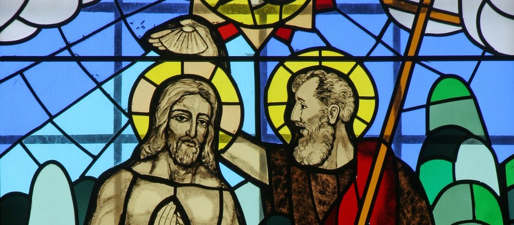 Szene auf einem bunten Kirchenfenster: Johannes tauft Jesus.