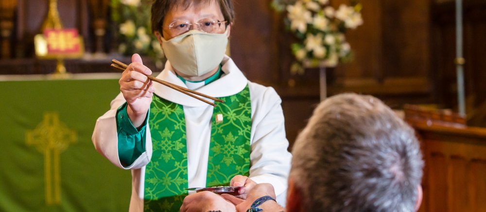 Rev. Eileen Harrop, Vikarin in der Diözese Durham im Nordosten Englands, teilt die Kommunion mit Essstäbchen aus.