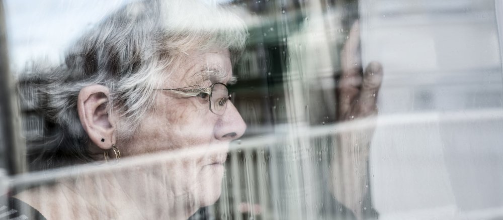 Eine Seniorin schaut traurig aus dem Fenster