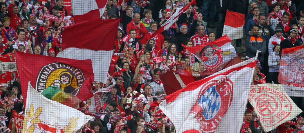 Hunderte Fans des FC Bayern München jubeln und schwenken im Stadion Vereinsfahnen.