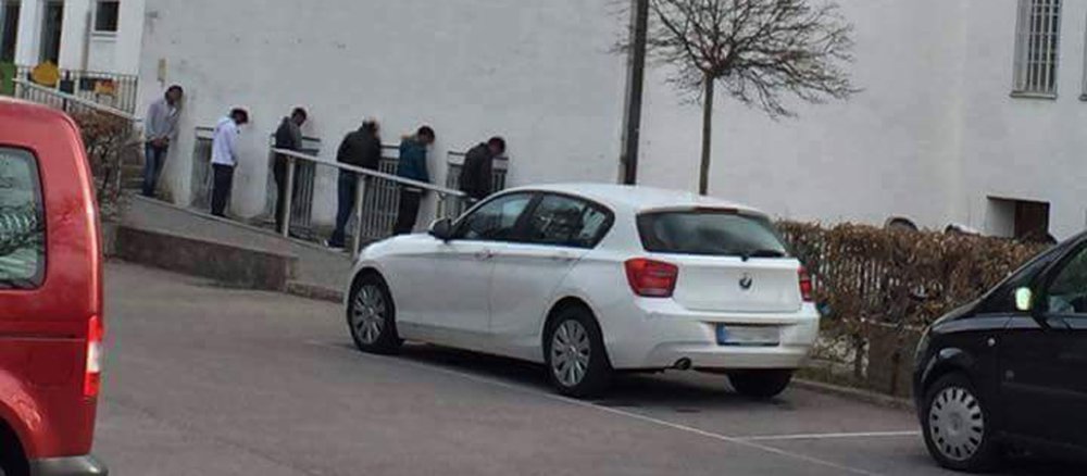 Sechs Menschen lehnen mit dem Kopf an einer Kirchenwand