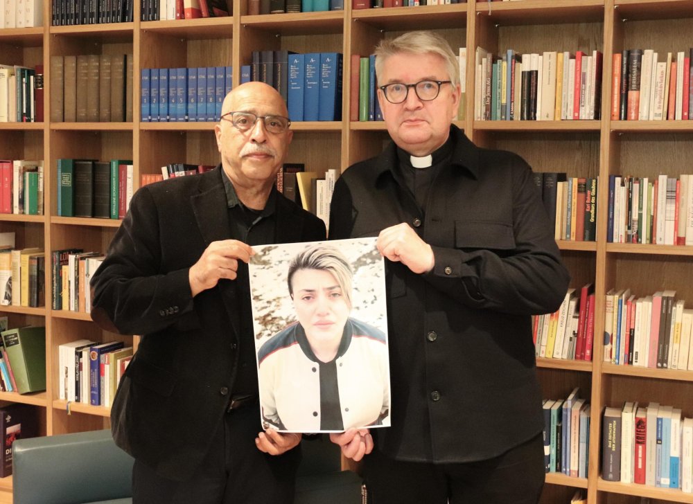 Behrouz Asadi (l) und Bischof Peter Kohlgraf halten ein Bild von Mahboubeh Shabani.