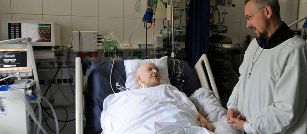 Pfarrer Walter Koll (Medizinische Universitäts-Poliklinik und Universitätsklinikum Bonn) spricht am Krankenbett mit einer Patientin.
