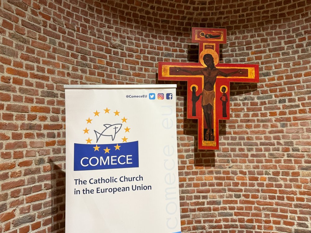 Aufsteller mit dem Logo der COMECE vor einem Kreuz