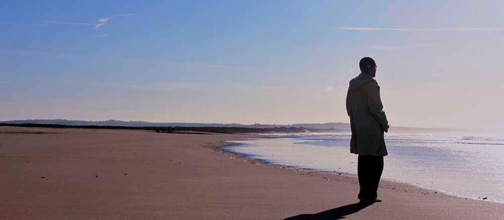 Ein einsamer Mann am Strand blickt nachdenklich auf das Meer.
