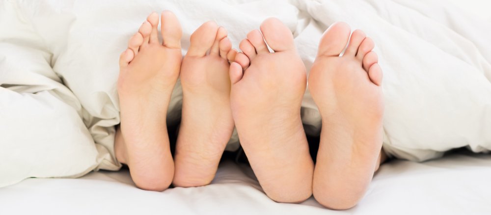 Frauenfüße und Männerfüße schauen unter einer Bettdecke hervor.