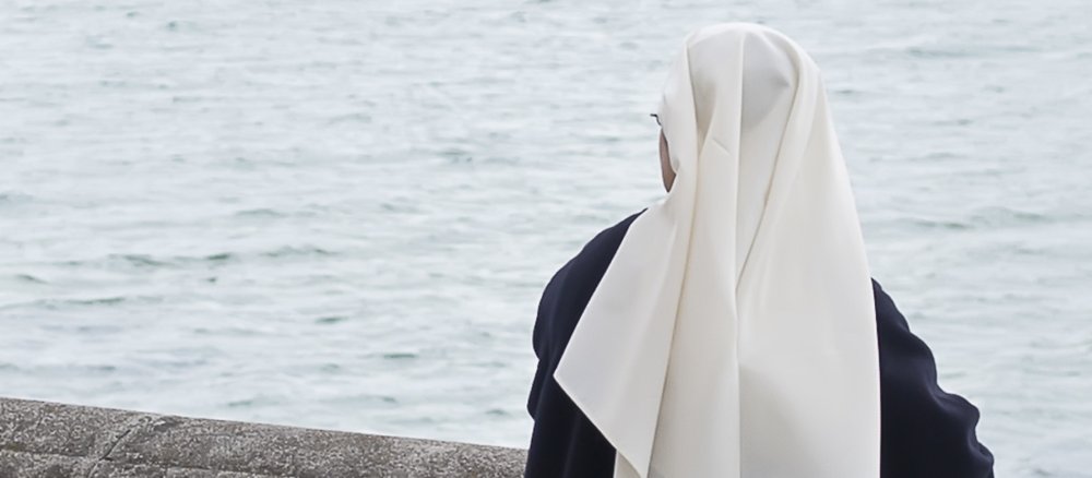 Eine Nonne steht am Meer.