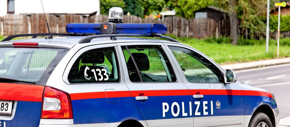 A patrol car (grey with blue and red trim) is parked on a country road.