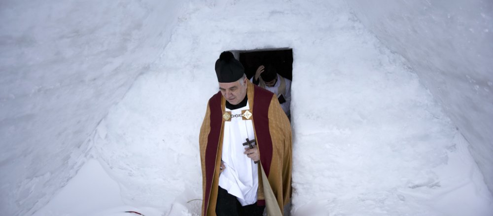 Ein Priester verlässt eine Kirche, die komplett aus Eisblocks und Schnee gebaut ist.