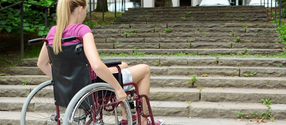 Eine Frau im Rollstuhl vor einer Treppe.