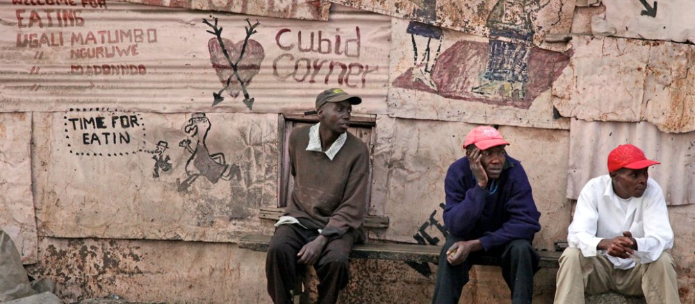 Drei Afrikaner sitzen vor einer Mauer mit Schriftzügen.