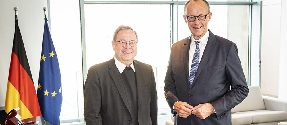 Bischof Georg Bätzing und Kanzler Friedrich Merz stehen neben den Flaggen der EU und Deutschlands