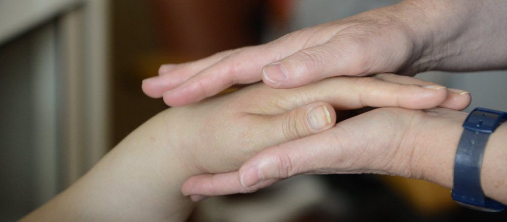 Eine Frau hält eine Hand zwischen ihren Händen.