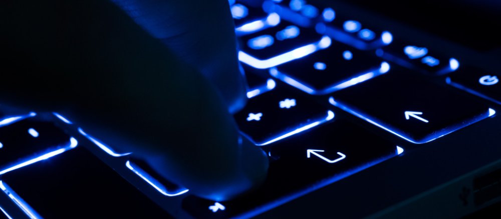 Ein Finger drückt die Enter-Taste auf einer blau beleuchteten Tastatur.