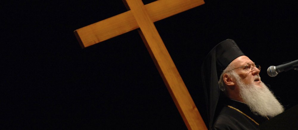 Patriarch Bartholomaios I. von Konstantinopel vor einem großen Holzkreuz.