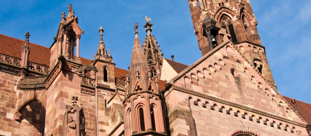 Vor blauem Himmel ist die seitliche Fassade einer rötlichen Sandsteinkirche zu sehen.